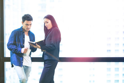 Colleagues discussing while standing by window in office