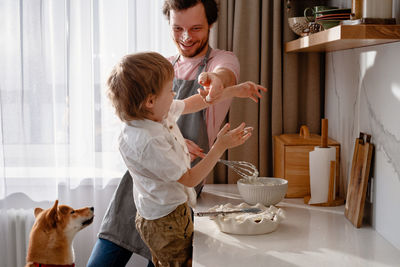 Dad holds a blender and plays with his little son and their dog. rubs his nose with whipped cream.