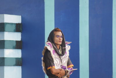 Portrait of a smiling young woman standing against blue wall