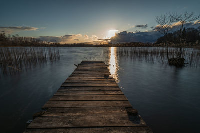 Pier over lake against sky during sunset