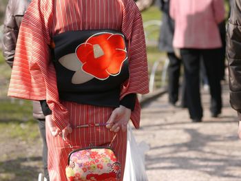 Midsection of woman wearing kimono holding purse on footpath