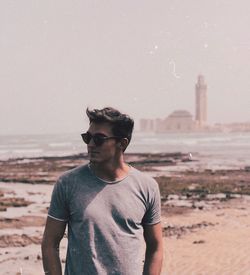 Young man wearing sunglasses standing on land against sea