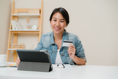 Portrait of smiling young woman using phone while sitting on table