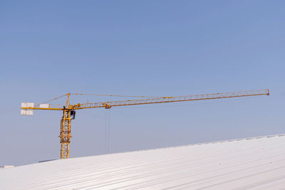 Low angle view of crane by building against clear sky