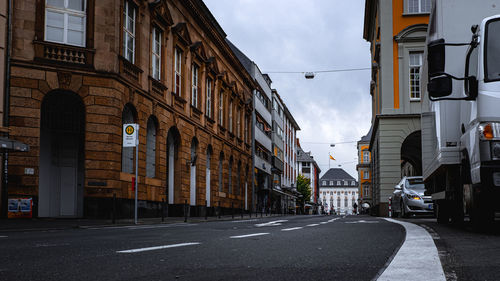 Road by buildings in city against sky