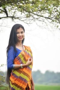Smiling young woman standing against plants