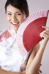 Portrait of smiling young woman holding hand fan against gray background