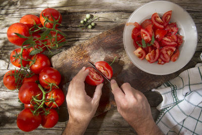 Cropped hands of man cutting cherry tomatoes on table