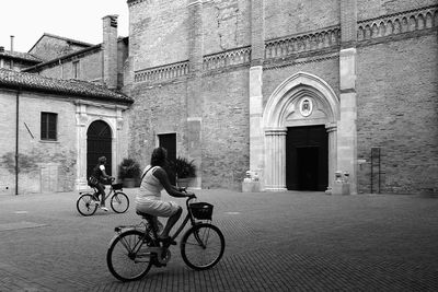 Rear view of women riding bicycles in front of historic building