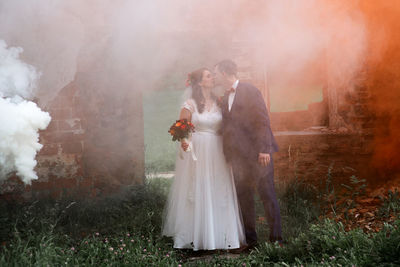 Full length of newlywed couple standing by abandoned built structure