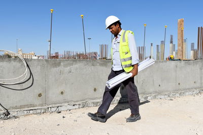 Man holding blueprints while walking at construction site