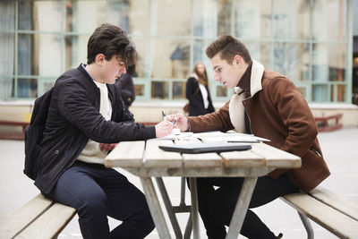 Male teenage friends studying at table in schoolyard