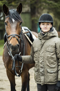 Portrait of young man with horse standing outdoors