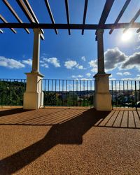 Shadow of railing on footpath against sky on sunny day