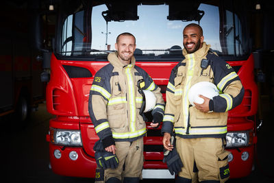 Portrait of coworkers standing in front of fire engine at fire station