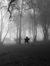 Rear view of silhouette girl on rope swing  in misty woodland