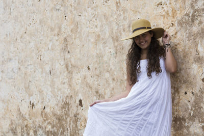 Portrait of smiling young woman standing against wall