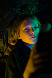 Portrait of tween looking at tablet with colorful light cast on face