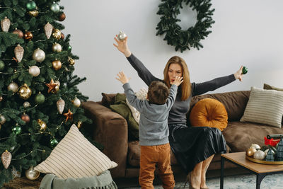 Mother with child playing near christmas tree. child unpacking gifts, woman enjoy christmas tree