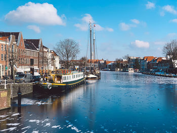 Sailboats moored in canal by buildings against sky