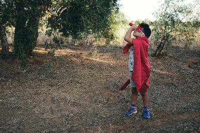 Child disguised as a red superhero takes his red spyglass to look for