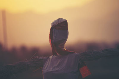 Rear view of woman standing against sky during sunset