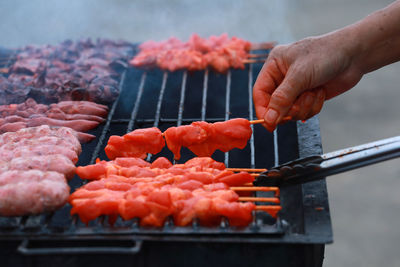 Cropped image of person preparing meat on barbecue grill