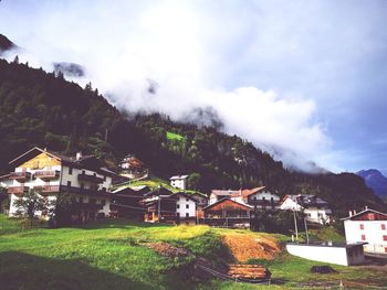 Houses on field by buildings against sky