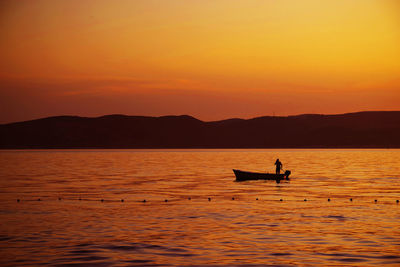 Silhouette boat on sea against orange sky