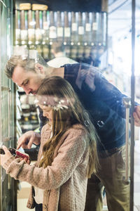 Side view of daughter holding juice bottle by father at refrigerator in supermarket