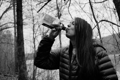 Young woman drinking glass with bare tree