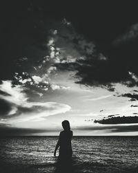 Silhouette boy standing at beach against sky