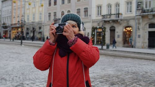 Man photographing woman with umbrella standing in city