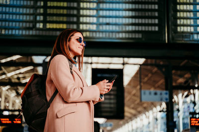 Woman with mobile phone standing at railroad station