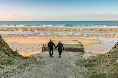 Rear view of couple holding hands while walking towards beach