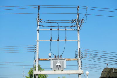 Low angle view of electricity transformer against clear blue sky