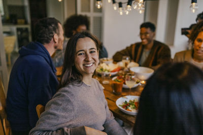 Portrait of smiling young woman sitting with friends at dining table