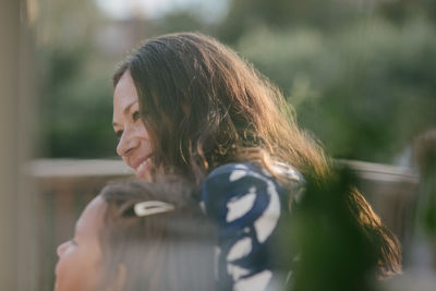 Smiling mid adult woman looking away while sitting with daughter on porch