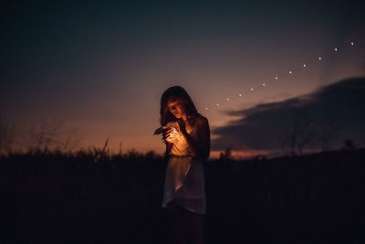 Woman standing on field against sky during sunset