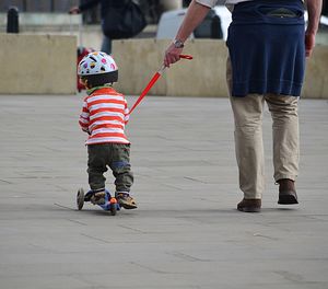 Rear view of son standing on push scooter with father on street
