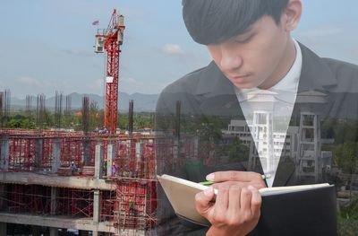 Double exposure image of man writing in diary and construction site