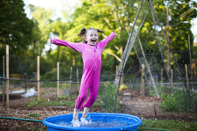 Cheerful girl jumping in wading pool on field
