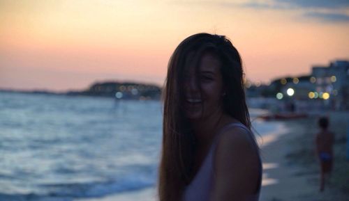 Close-up of smiling young woman at beach against sky during sunset
