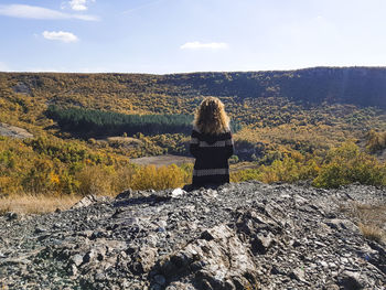 Rear view of woman sitting on field against sky