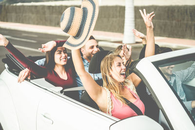 Happy friends with arms raised traveling in convertible