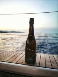 Glass bottle on table by sea against sky