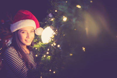 Portrait of smiling woman by illuminated christmas tree at night