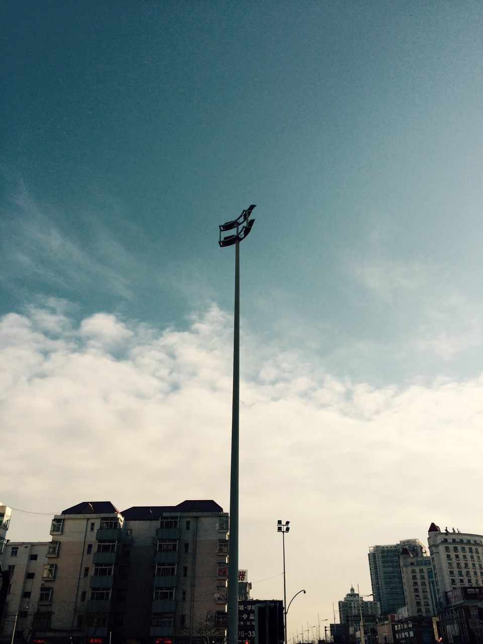 building exterior, architecture, low angle view, built structure, street light, sky, city, building, cloud - sky, cloud, lighting equipment, residential building, outdoors, day, residential structure, pole, no people, blue, high section, tall - high