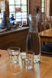 Jug with drinking glasses on wooden table at bar