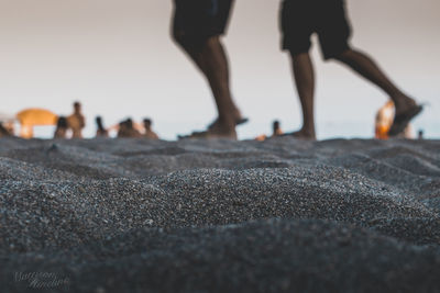 Low section of people walking on sand at beach